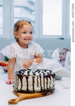 a little girl in a dress is preparing to blow out a candle on a birthday cake 64872000