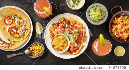 Mexican food, a flat lay panorama on a dark background. Nachos, tortillas, Paloma cocktails, guacamole and other dishes, shot from above 64873806