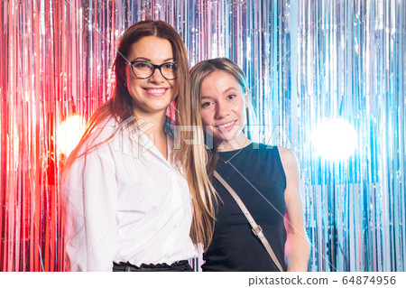 Portrait of two attractive happy women in evening dresses hugging and looking at camera isolated over silver coloured shiny background. Birthday party, holidays and night club concept. Portrait of two attractive happy women in evening dresses hugging and looking at camera isolated over silver coloured shiny background. Birthday party, holidays and night club concept. 64874956