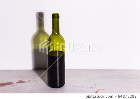 Bottle with wine, red puddle of wine on the table. Cleaning after party concept. Bottle with wine, red puddle of wine on the table. Cleaning after party concept. 64875292