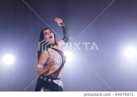 Young woman belly dancer in exotic dress with gold, dancing tribal fusion dance in studio. Copy space. 64876072