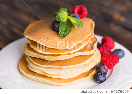 Pancakes with blueberries and raspberry on wooden background. Breakfast and traditional meal. Pancakes with blueberries and raspberry on wooden background. Breakfast and traditional meal. 64876995