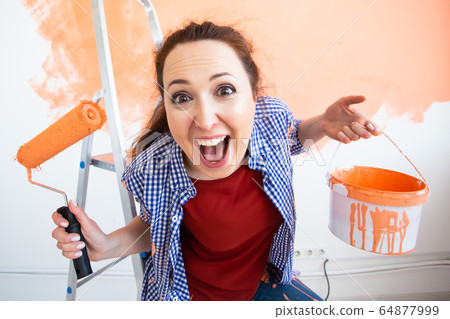 Renovation, redecoration and repair concept - Funny woman painting wall in new home. Renovation, redecoration and repair concept - Funny woman painting wall in new home. 64877999