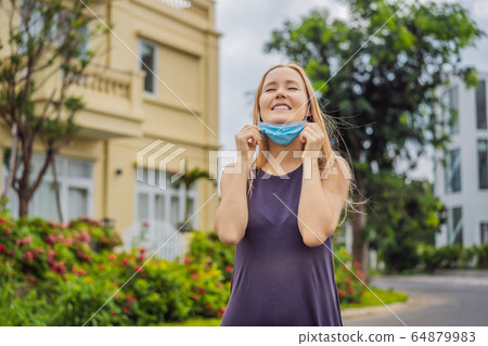 Quarantine is over concept. Woman taking off mask against the background of small town houses. We 64879983