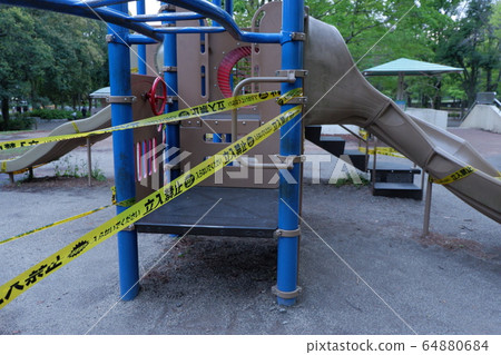 A park forbidden to enter due to the new coronavirus. A yellow prohibition tape on playground equipment is prohibited due to an emergency declaration. A park forbidden to enter due to the new coronavirus. A yellow prohibition tape on playground equipment is prohibited due to an emergency declaration. 64880684