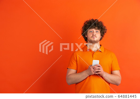 Caucasian young man's monochrome portrait on orange studio background Caucasian young man's monochrome portrait on orange studio background 64881445