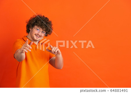 Caucasian young man's monochrome portrait on orange studio background Caucasian young man's monochrome portrait on orange studio background 64881491