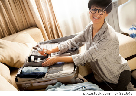 Open grey suitcase with different clothes packed for journey at home. Nordic style minimalism. woman packing bags for holidays and preparing things for vacations getting ready for travel 64881643