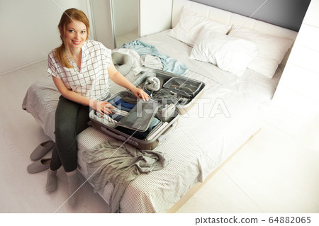 Open grey suitcase with different clothes packed for journey at home. Nordic style minimalism. woman packing bags for holidays and preparing things for vacations getting ready for travel 64882065