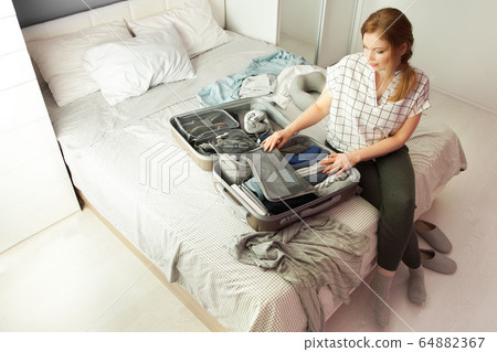 Open grey suitcase with different clothes packed for journey at home. Nordic style minimalism. woman packing bags for holidays and preparing things for vacations getting ready for travel Open grey suitcase with different clothes packed for journey at home. Nordic style minimalism. woman packing bags for holidays and preparing things for vacations getting ready for travel 64882367