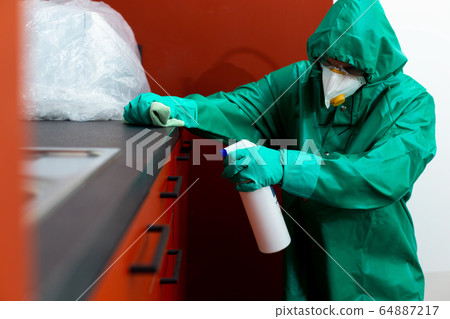 Man in protective suit spraying chemicals on kitchen cabinetry 64887217