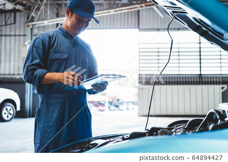 Car mechanic holding clipboard and checking to 64894427