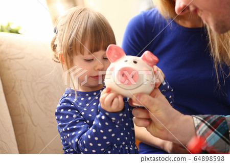 Child little girl arm putting coins into piggybank Child little girl arm putting coins into piggybank 64898598