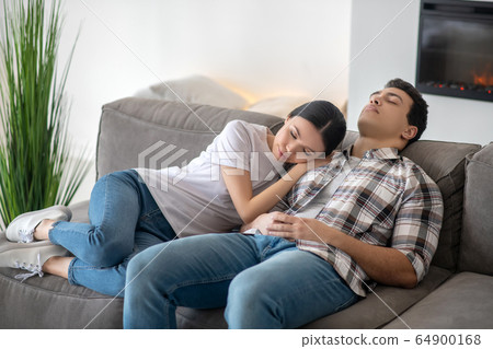 Dark-haired female resting her head on brunette male shoulder, both resting on sofa 64900168