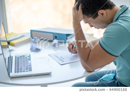Dark-haired male sitting at his desk, filling in unemployment claim 64900188
