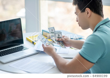 Dark-haired male sitting at his desk, calculating money Dark-haired male sitting at his desk, calculating money 64900199