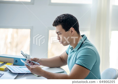 Sad dark-haired male sitting at his desk, calculating money 64900205