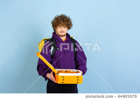 Contacless delivery service during quarantine. Man delivers food and shopping bags during insulation. Emotions of deliveryman isolated on blue background. Contacless delivery service during quarantine. Man delivers food and shopping bags during insulation. Emotions of deliveryman isolated on blue background. 64905079