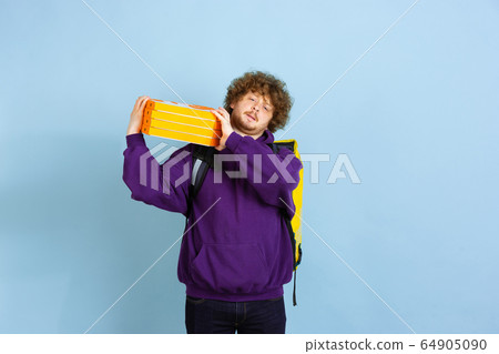 Contacless delivery service during quarantine. Man delivers food and shopping bags during insulation. Emotions of deliveryman isolated on blue background. Contacless delivery service during quarantine. Man delivers food and shopping bags during insulation. Emotions of deliveryman isolated on blue background. 64905090