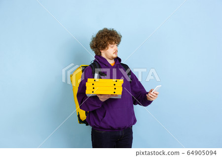 Contacless delivery service during quarantine. Man delivers food and shopping bags during insulation. Emotions of deliveryman isolated on blue background. Contacless delivery service during quarantine. Man delivers food and shopping bags during insulation. Emotions of deliveryman isolated on blue background. 64905094