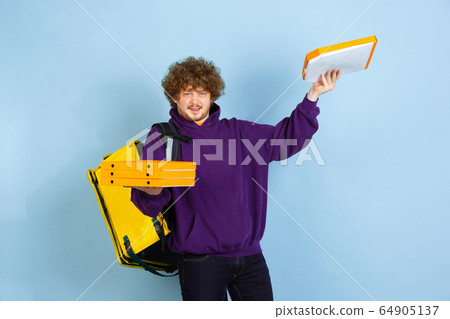 Contacless delivery service during quarantine. Man delivers food and shopping bags during insulation. Emotions of deliveryman isolated on blue background. Contacless delivery service during quarantine. Man delivers food and shopping bags during insulation. Emotions of deliveryman isolated on blue background. 64905137