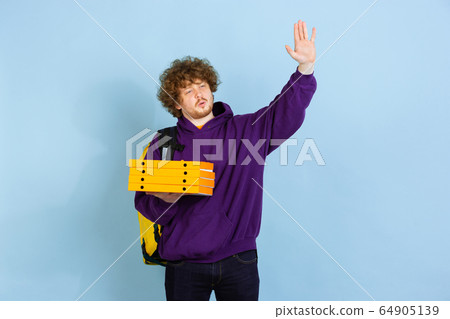 Contacless delivery service during quarantine. Man delivers food and shopping bags during insulation. Emotions of deliveryman isolated on blue background. Contacless delivery service during quarantine. Man delivers food and shopping bags during insulation. Emotions of deliveryman isolated on blue background. 64905139
