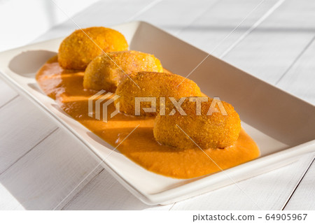 Fried meat croquettes with vegetable cream sauce on white plate at sunny kitchen. Side view on white wooden background. Fried meat croquettes with vegetable cream sauce on white plate at sunny kitchen. Side view on white wooden background. 64905967