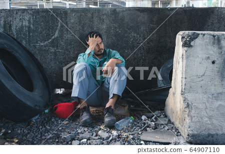 Homeless man sitting sadly beside the wall 64907110