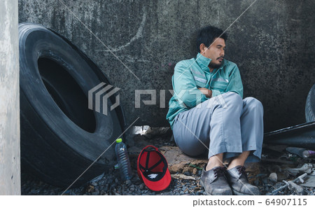 Homeless man sitting sadly beside the wall 64907115