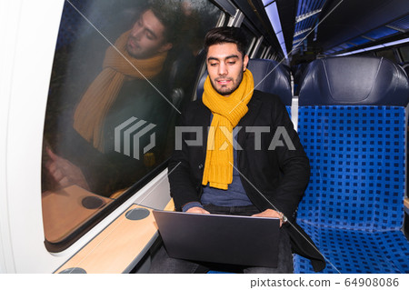 Arab man in train holds laptop and looks at camera Arab man in train holds laptop and looks at camera 64908086