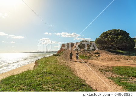 Two girls athletes in sports uniforms, walk along the cliff shore, in the summer near the sea. Beach of Falesia, Vilamoura Albufeira, Portugal. 64908825