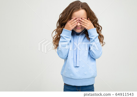 European teenage girl in a blue hoodie covered her eyes with her hands on a white background with 64911543