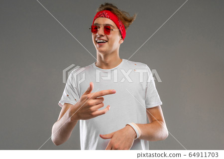 Young caucasian man in red sunglasses, white t-shirt posing on camera isolated on grey background Young caucasian man in red sunglasses, white t-shirt posing on camera isolated on grey background 64911703