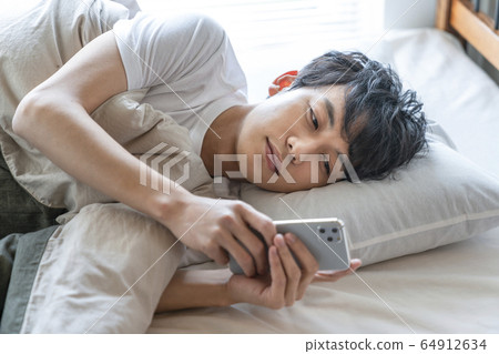 Young man looking at smartphone while sleeping in bed Young man looking at smartphone while sleeping in bed 64912634