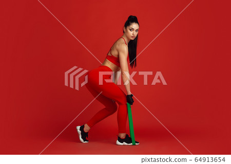 Beautiful young female athlete practicing on red studio background, monochrome portrait 64913654