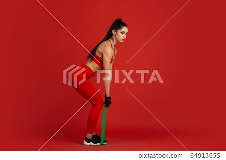 Beautiful young female athlete practicing on red studio background, monochrome portrait 64913655
