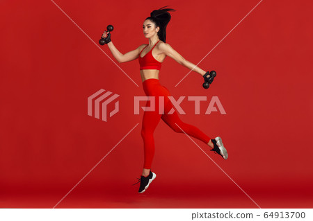 Beautiful young female athlete practicing on red studio background, monochrome portrait 64913700