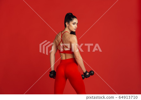 Beautiful young female athlete practicing on red studio background, monochrome portrait Beautiful young female athlete practicing on red studio background, monochrome portrait 64913710