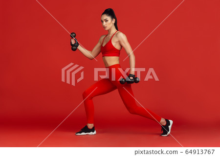 Beautiful young female athlete practicing on red studio background, monochrome portrait Beautiful young female athlete practicing on red studio background, monochrome portrait 64913767