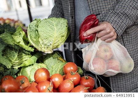 man using reusable mesh bags at a greengrocer 64913951