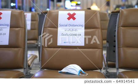 Medical mask on a chair with signed about Social distancing in airport to protect corona virus 64914541