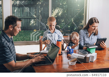 Concept of work from home and home family education. Parents and two sons are sitting at the desk. Concept of work from home and home family education. Parents and two sons are sitting at the desk. 64917110