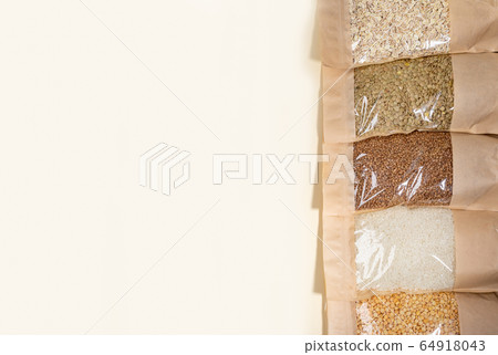 Paper - cellophane bags with cereals and legumes laid out in row on beige backdrop. Copy space. Buckwheat, peas, lentils, rice, oat flakes. Zero Waste Food Storage. No plastic. Stock for a rainy day. 64918043