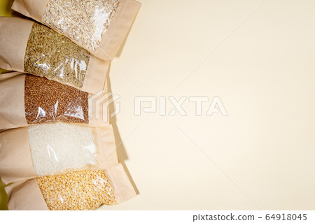 Paper - cellophane bags of cereals, legumes close-up on beige backdrop with copy space. Buckwheat, peas, lentils, rice, oat flakes. Zero Waste Food Storage Concept. No plastic. Stock for a rainy day. 64918045
