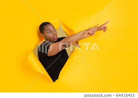 Cheerful young woman poses in torn yellow paper hole background, emotional and expressive Cheerful young woman poses in torn yellow paper hole background, emotional and expressive 64918453