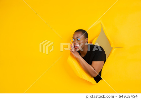 Cheerful young woman poses in torn yellow paper hole background, emotional and expressive Cheerful young woman poses in torn yellow paper hole background, emotional and expressive 64918454