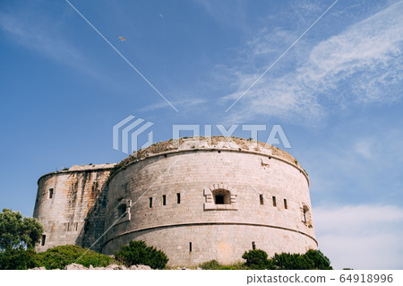 The ancient Austro-Hungarian fort Arza at the entrance to the Bay of Kotor in Montenegro, in the Adriatic Sea, on Lustica peninsula. Fortress for military defense. Stone tower built in 19th century. The ancient Austro-Hungarian fort Arza at the entrance to the Bay of Kotor in Montenegro, in the Adriatic Sea, on Lustica peninsula. Fortress for military defense. Stone tower built in 19th century. 64918996