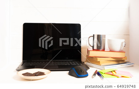 Home office concept. Work from home. Black laptop, books and cafe cuo on the white wooden background. Side view.  64919748