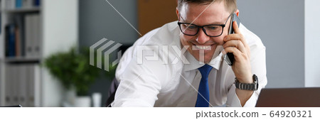 Joyful man in office speaks on phone near laptop Joyful man in office speaks on phone near laptop 64920321
