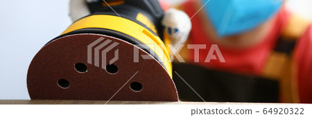Masked carpenter grinds wood with sander machine Masked carpenter grinds wood with sander machine 64920322
